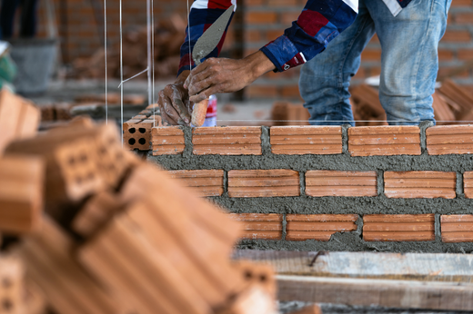 Image shows masonry contractor working on a brick wall